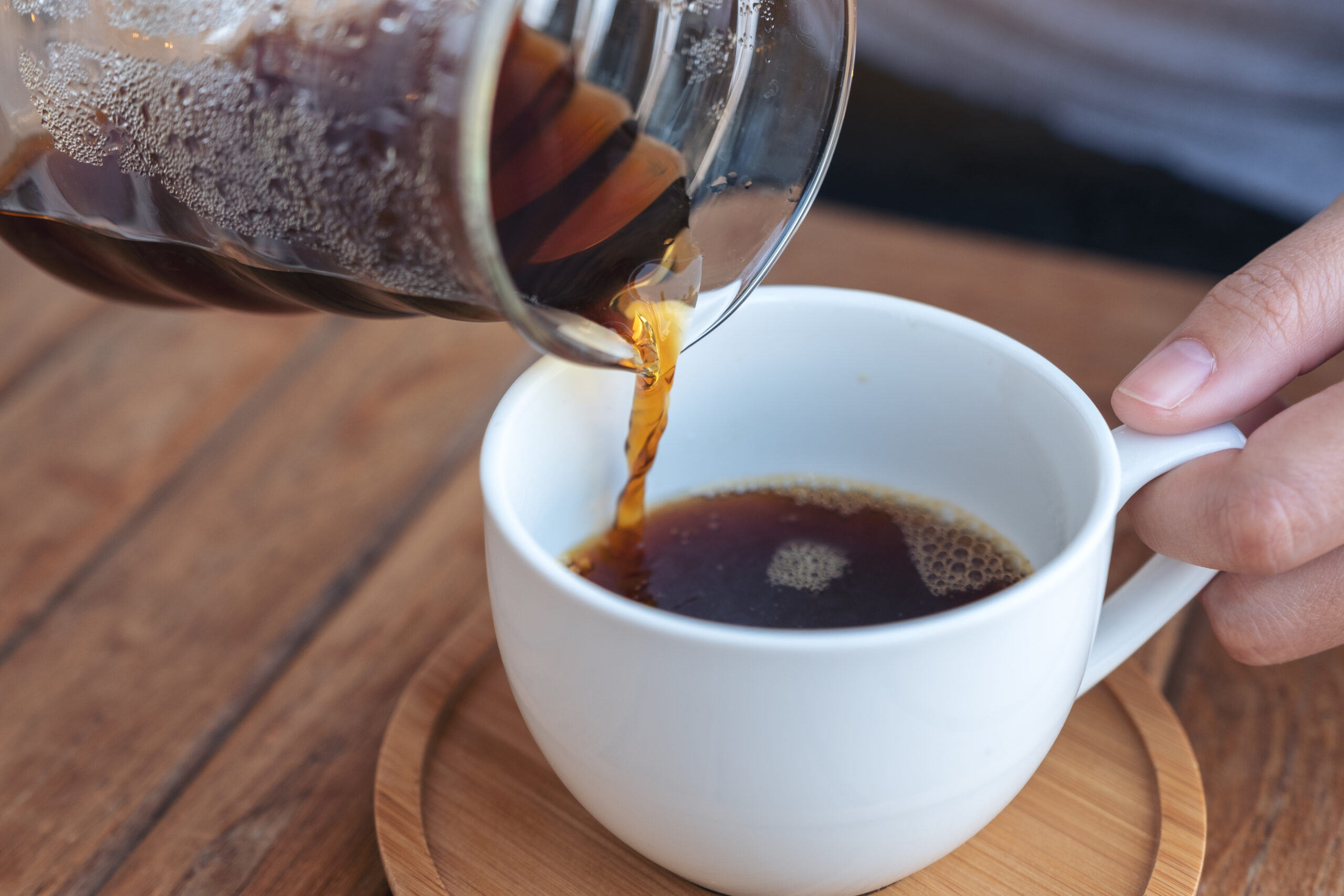 Closeup image of a hand pouring drip coffee into a white mug on vintage wooden table